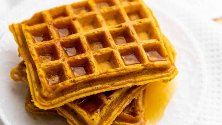 Close-up of two stacked waffles on a white plate with syrup pooled in some of the waffle squares.