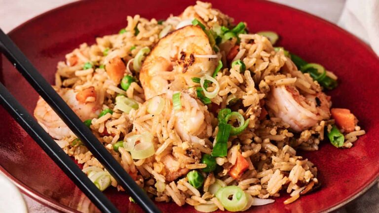 A plate of shrimp fried rice with chopped green onions and vegetables, served with black chopsticks on the side.