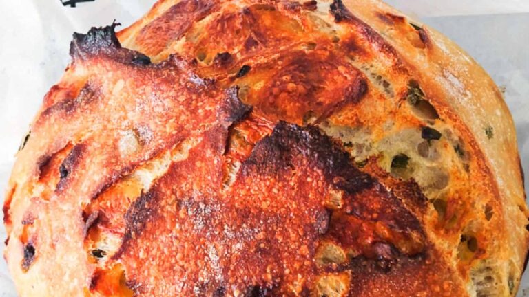 A close-up of a round loaf of rustic bread with a golden-brown, crispy crust and visible air pockets.