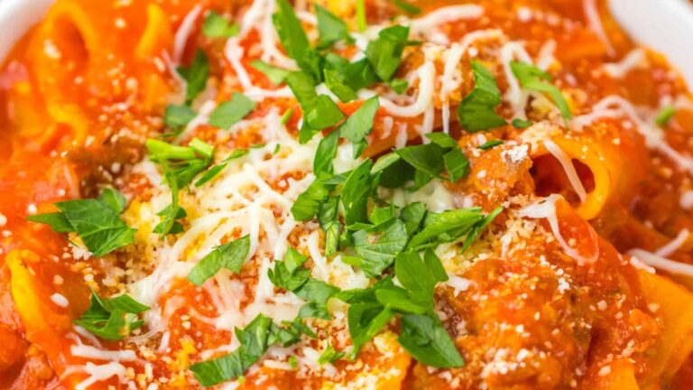 A close-up of pasta topped with tomato sauce, grated cheese, ground meat, and fresh chopped parsley.