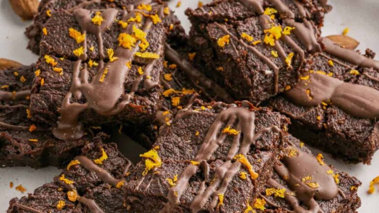 A close-up of several sweet potato brownies drizzled with chocolate and sprinkled with orange zest, arranged on a white surface.