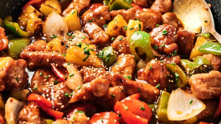 Close-up of sweet and sour chicken with bell peppers, onions, pineapple, and sesame seeds in a glossy sauce.