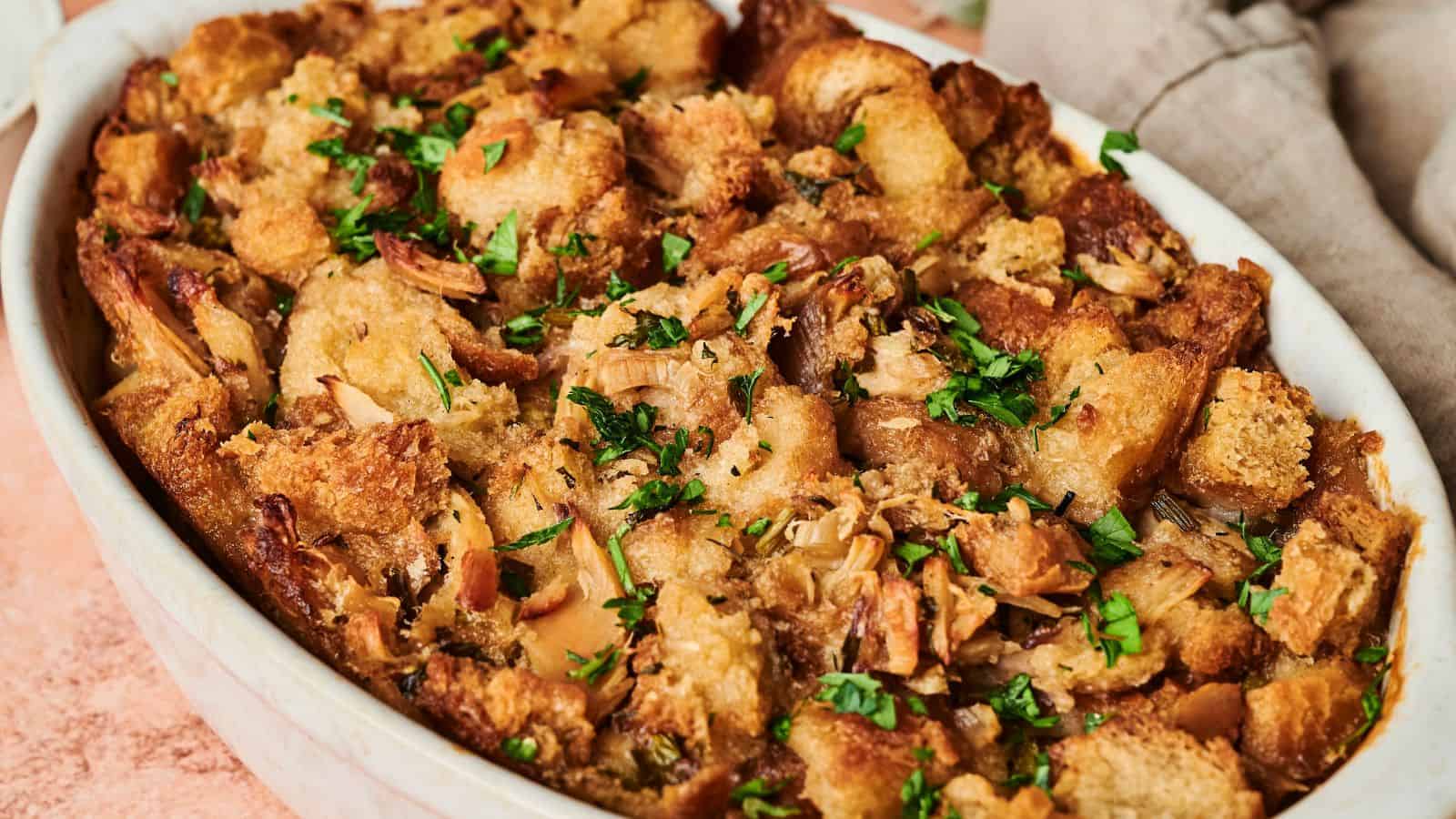A golden brown Thanksgiving casserole of baked stuffing garnished with fresh herbs.