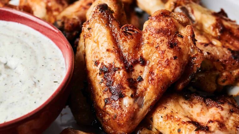 Close-up of grilled chicken wings next to a bowl of creamy dipping sauce.
