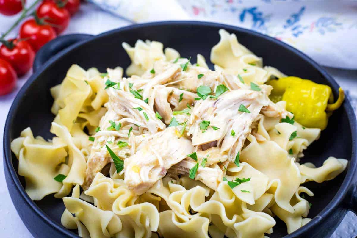 Mississippi Chicken - Slow Cooker with herbs and two yellow peppers on a white rectangular plate.