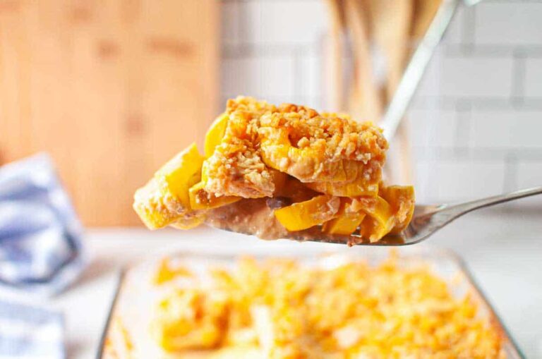 A close-up of a serving of cheesy baked yellow squash casserole on a metal spatula, with the casserole dish in the background.