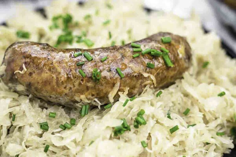 A grilled sausage rests on a bed of sauerkraut, garnished with chopped chives.