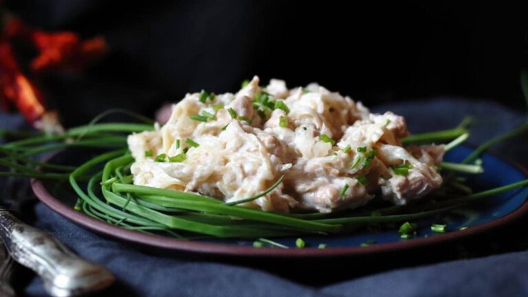 A plate of creamy chicken salad garnished with chopped chives and surrounded by fresh chive stems on a dark background.