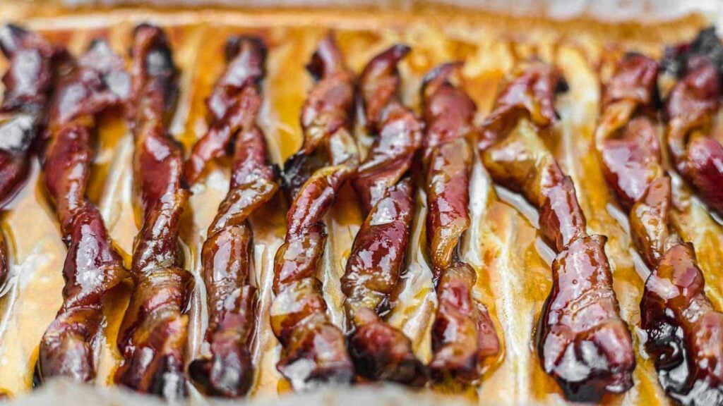Close-up of cooked bacon strips arranged in rows on a baking tray, glistening with rendered fat.