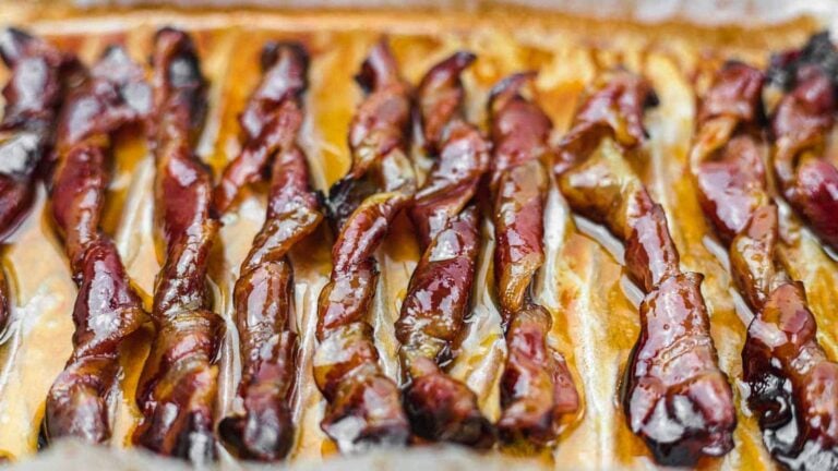 Close-up of cooked bacon strips arranged in rows on a baking tray, glistening with rendered fat.