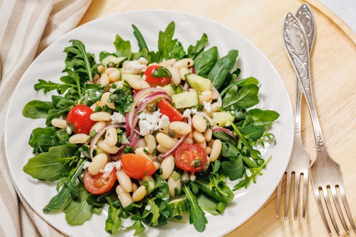 A plate of white bean salad on a wooden surface next to two vintage forks.
