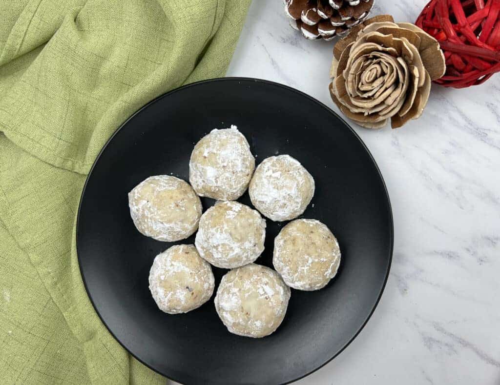 Top-down shot of seven pecan butter balls on a black plate.