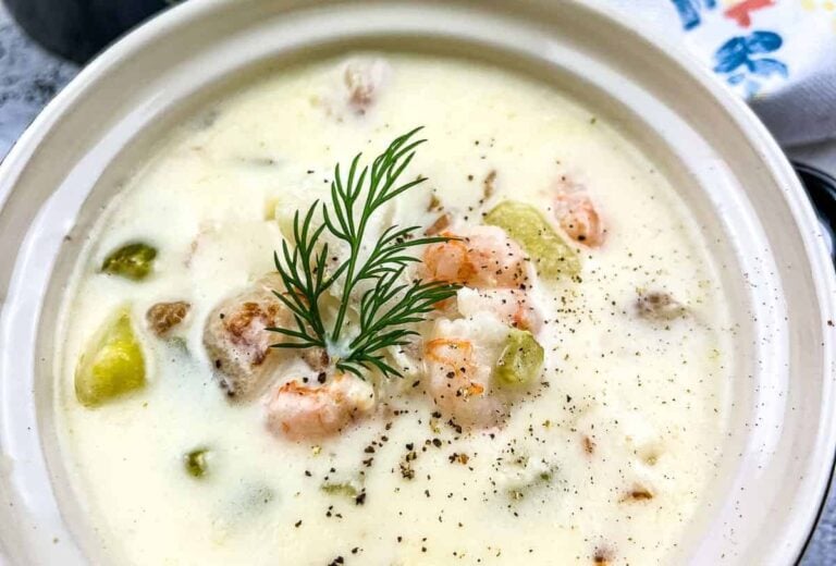 A bowl of creamy seafood chowder with shrimp, vegetables, and a sprig of dill, topped with black pepper.