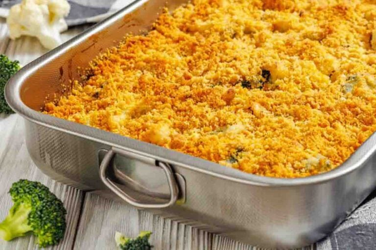 A stainless steel baking dish filled with baked broccoli casserole topped with a golden breadcrumb crust, sitting on a wooden table.