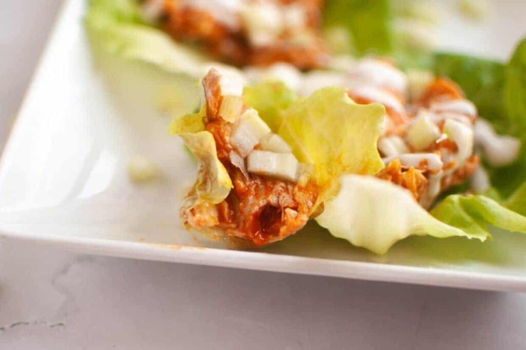 A close-up of a lettuce wrap filled with shredded meat, diced onions, and sauce on a white plate.