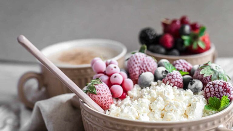 A bowl of cottage cheese topped with frozen berries, next to a cup of coffee and another bowl of mixed berries.