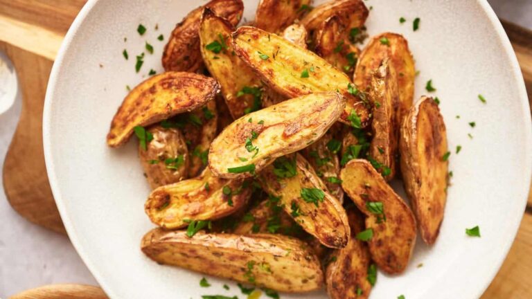 A white bowl filled with roasted potato wedges garnished with chopped parsley.
