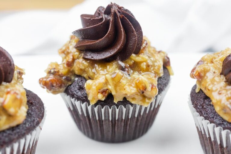 A chocolate cupcake topped with a layer of coconut pecan frosting and a swirl of chocolate icing, displayed on a white surface.