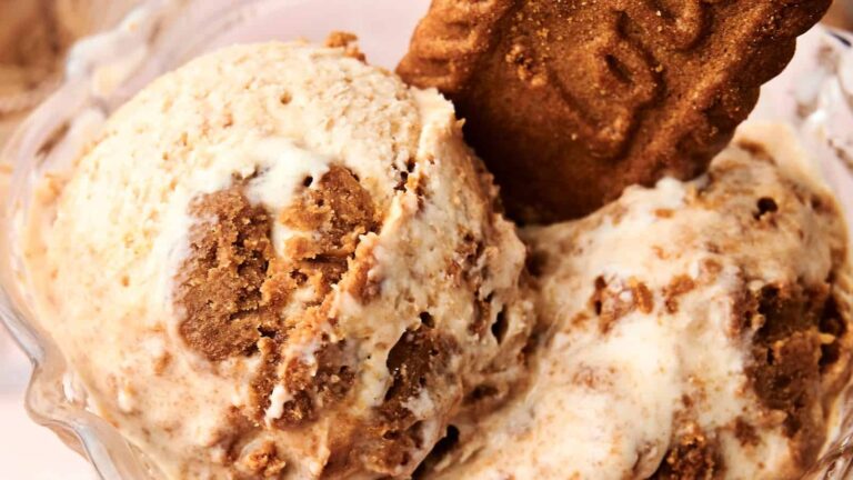 Scoops of ice cream with chunks of cookie and a whole cookie piece placed on top in a glass bowl.