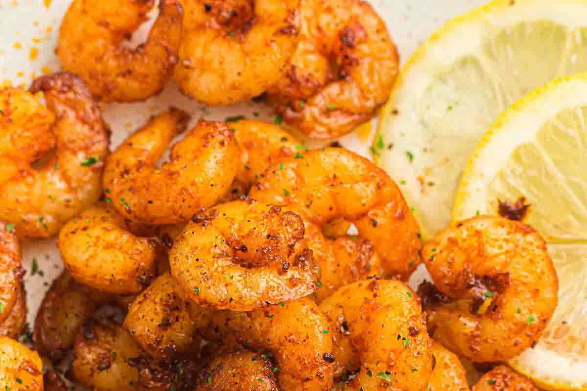 Cooked shrimp seasoned with spices, served on a plate next to two lemon slices.