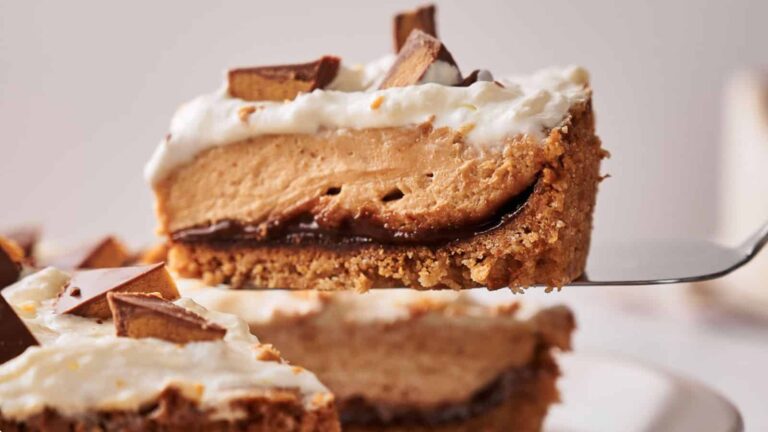 A close-up of a slice of pie with a cookie crust, chocolate layer, peanut butter filling, whipped topping, and chocolate pieces on top.