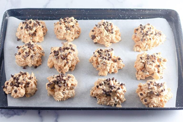 A baking tray lined with parchment paper holds twelve Avalanche Crunch Cookies.
