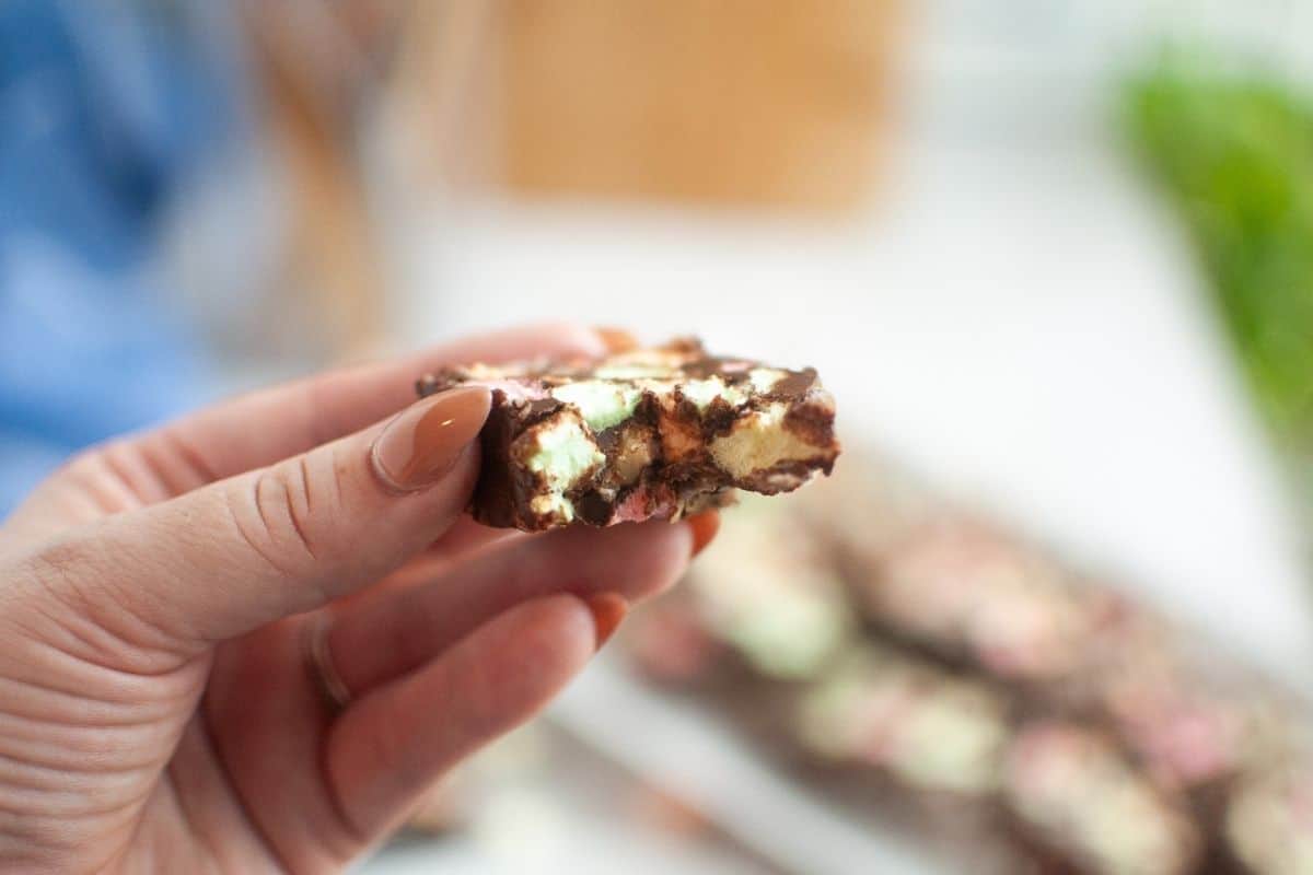 A hand holding a piece of Church Window Cookies, with more pieces blurred in the background.