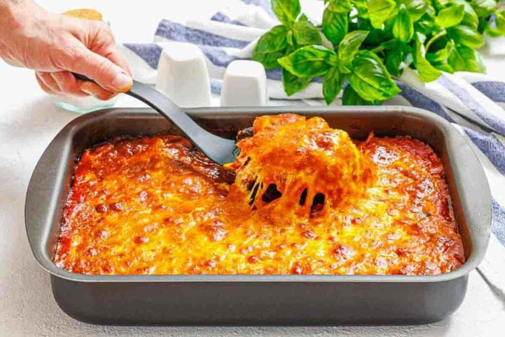 Spoon lifting melted cheesy eggplant parmesan serving.