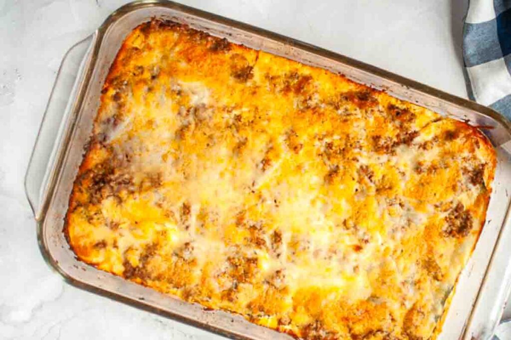 A baked casserole with a golden-brown, cheesy top and visible ground meat in a rectangular glass dish on a light surface.