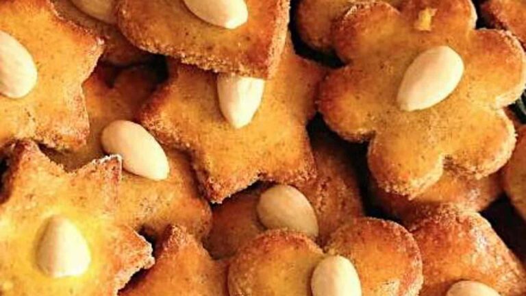 Close-up of various-shaped cookies topped with whole almonds, stacked together.