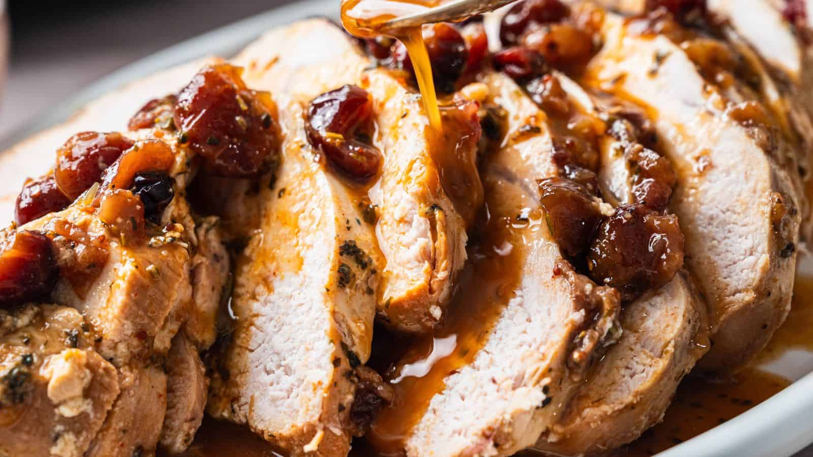 Sliced roasted turkey breast topped with a fruit-based sauce, being drizzled with additional sauce from a spoon.