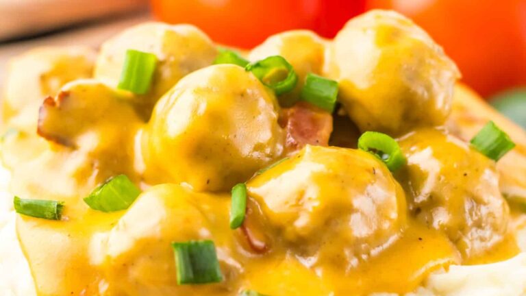 A close-up of meatballs covered in yellow gravy, garnished with chopped green onions.