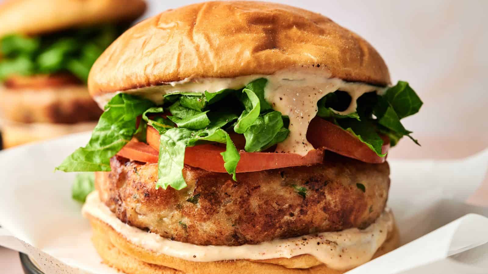 A close-up of a chicken burger with lettuce, tomato, and a creamy sauce in a toasted bun.