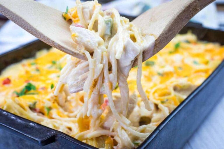 A wooden utensil lifts a portion of cheesy baked spaghetti from a rectangular baking dish.