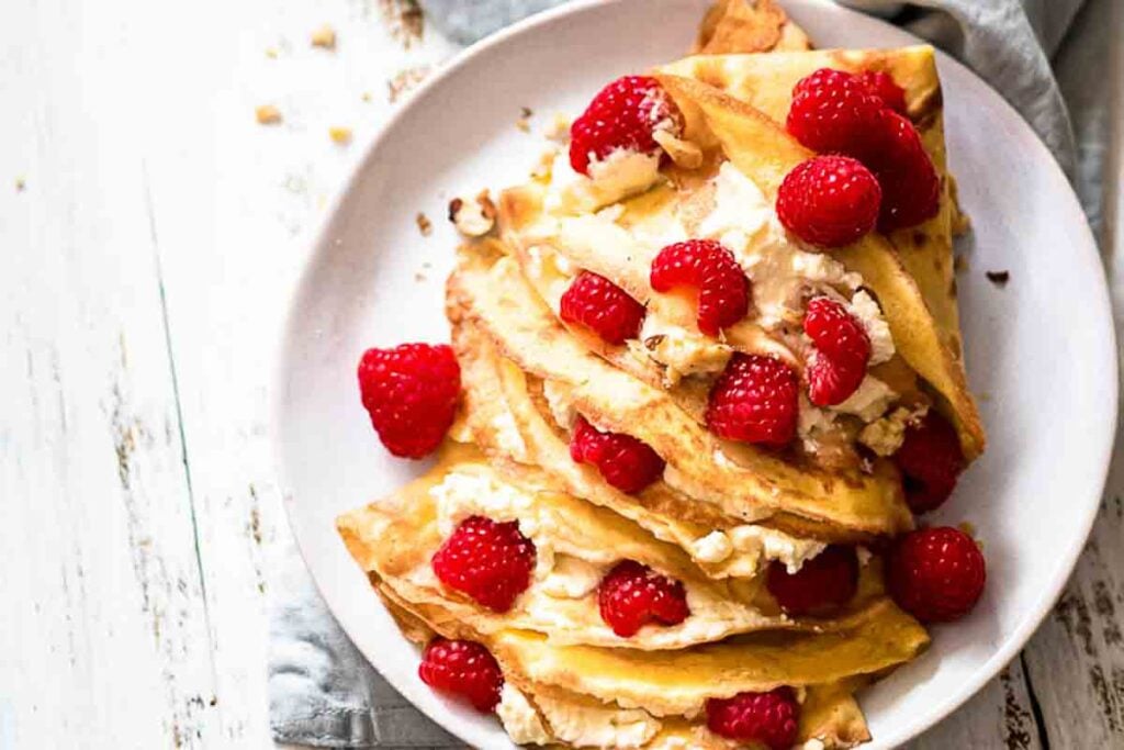 Plate of folded crepes with raspberries filling.