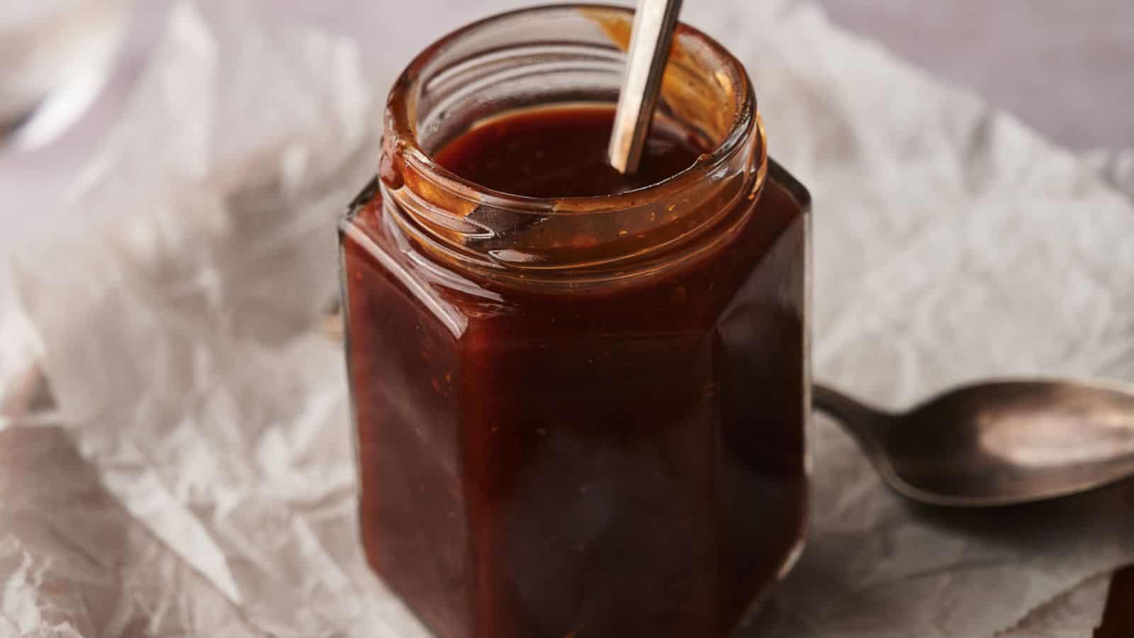 Homemade BBQ sauce in a jar with two spoons by the side.
