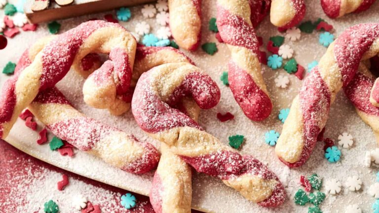 Red and white twisted candy cane cookies dusted with powdered sugar, surrounded by festive snowflake and tree-shaped sprinkles.