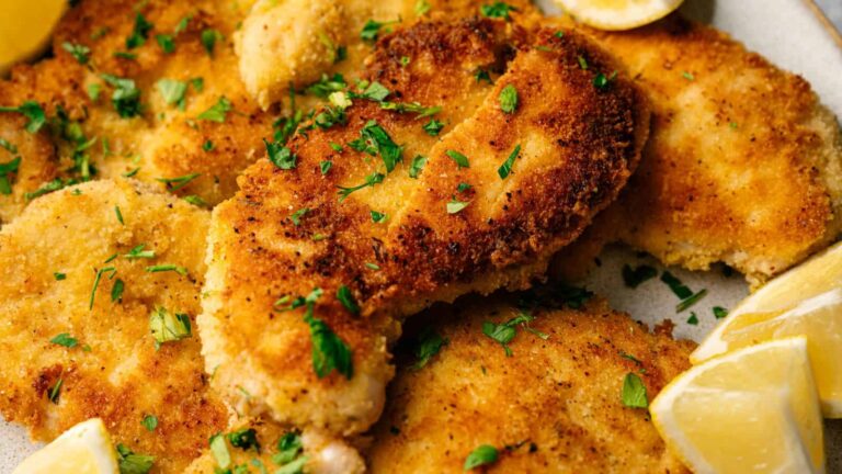 Breaded and fried chicken cutlets garnished with chopped parsley, served with lemon wedges on the side.