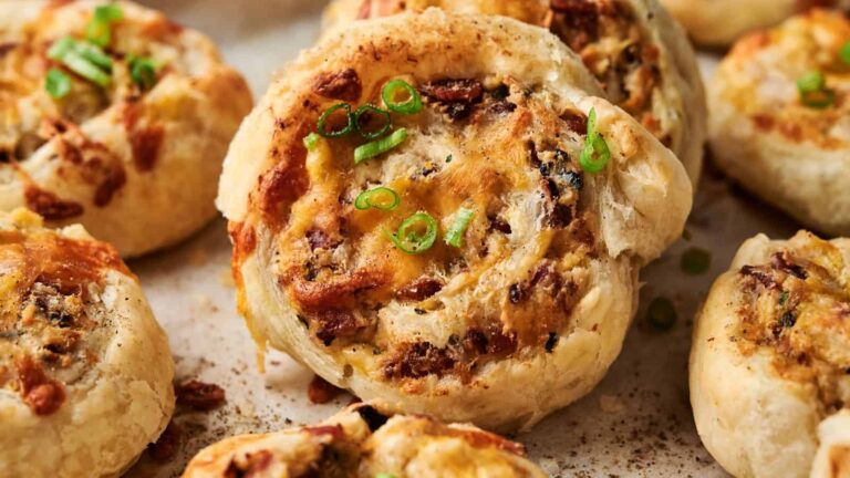 A close-up of baked savory pinwheel pastries topped with chopped green onions on a parchment-lined surface.