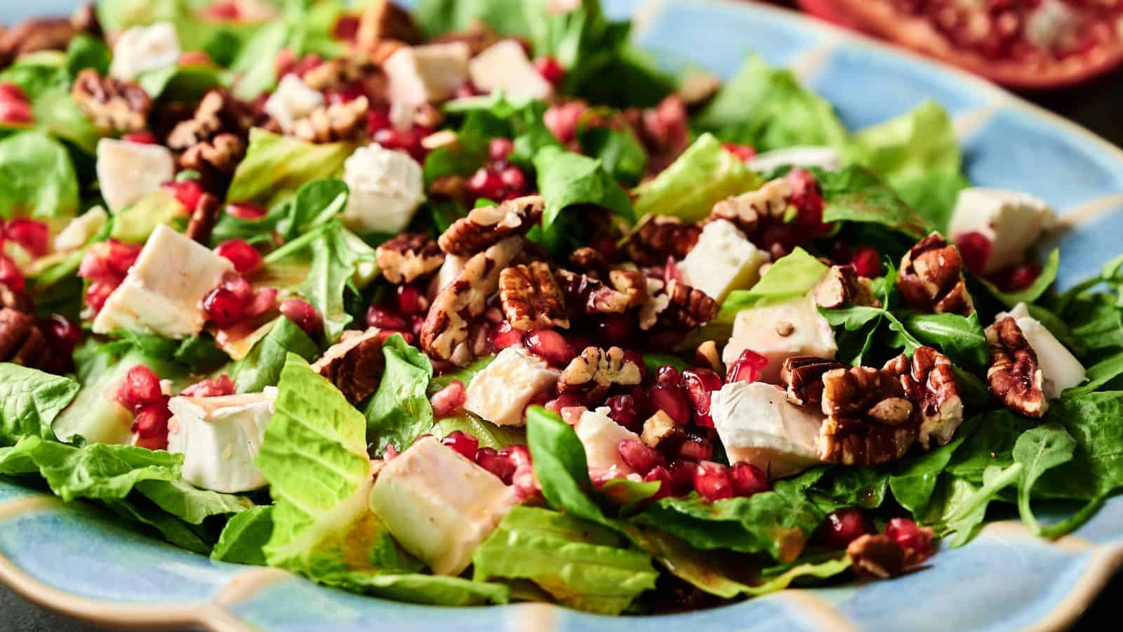 A close-up of a salad with chopped romaine lettuce, diced white cheese, pecans, and pomegranate seeds on a blue plate.