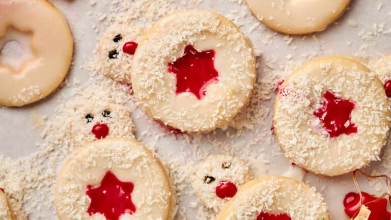 Round cookies with a red jam star center and white icing are arranged on a surface, sprinkled with shredded coconut.