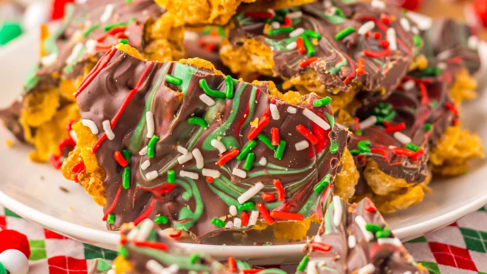 Chocolate bark with red, green, and white sprinkles on a plate, festive decorations in the background.