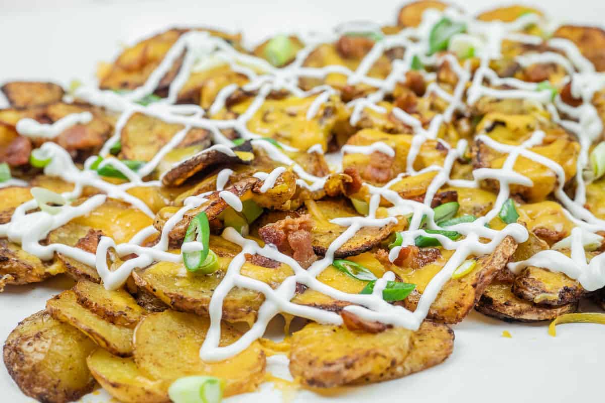 A platter of Air Fryer Irish Nachos topped with melted cheese, sour cream, bacon bits, and chopped green onions.