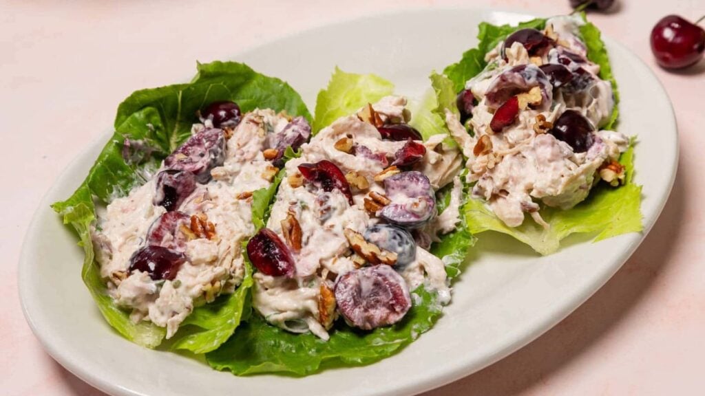 Three lettuce leaves topped with a creamy chicken salad containing grapes and pecans, served on a white plate.