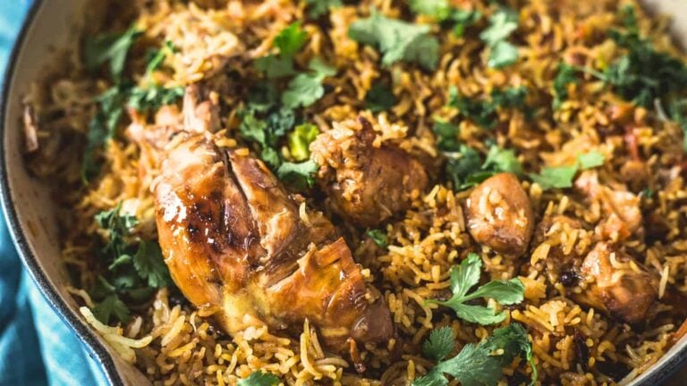 Cooked chicken and spiced rice garnished with fresh cilantro in a large pan.