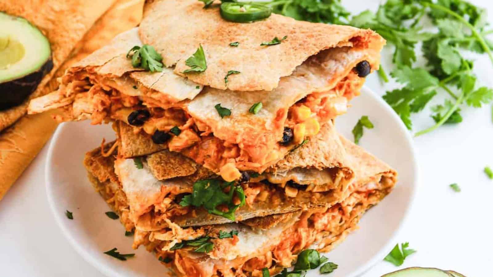 Stack of chicken quesadilla wedges with cilantro garnish.