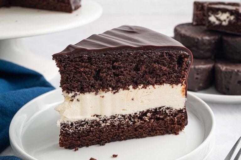 A slice of chocolate cake with a thick vanilla cream filling and glossy chocolate frosting on a white plate—perfect inspiration for tasty cake recipes.