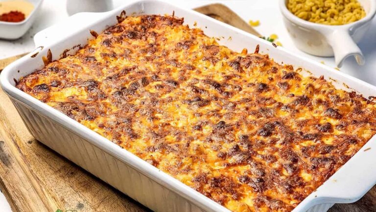A baking dish filled with baked macaroni and cheese, with a browned, crispy cheese topping, sits on a wooden board.