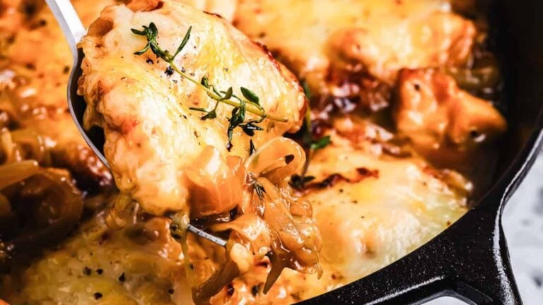 A close-up of a cheesy baked dish with caramelized onions and herbs being served from a skillet.