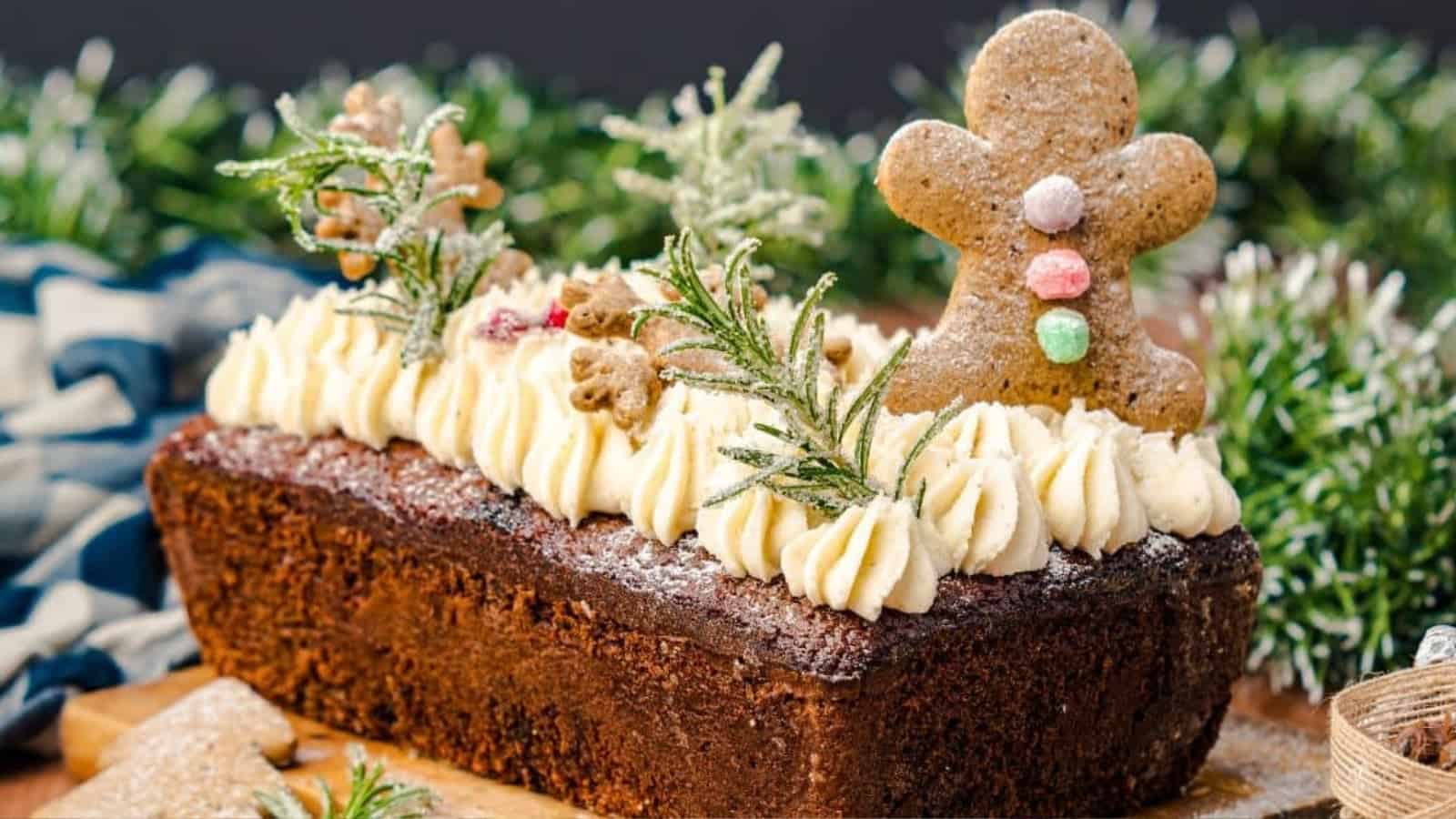 A festive loaf cake topped with icing, rosemary sprigs, and gingerbread men decorations.
